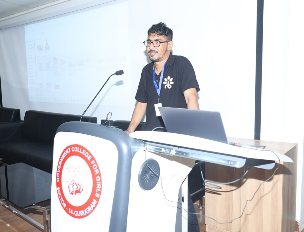 A man in a black shirt confidently stands at a podium, holding a laptop while addressing an audience.