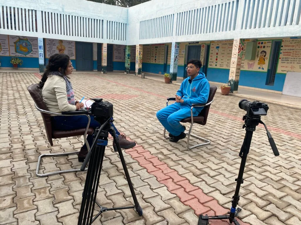 A boy sitting on a chair in front of a lady. and both are facing the camera.